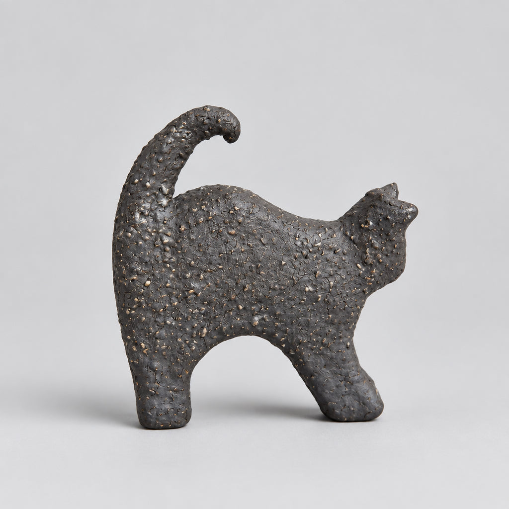 A small dark textured cat figurine standing on a wooden surface, made of black clay.