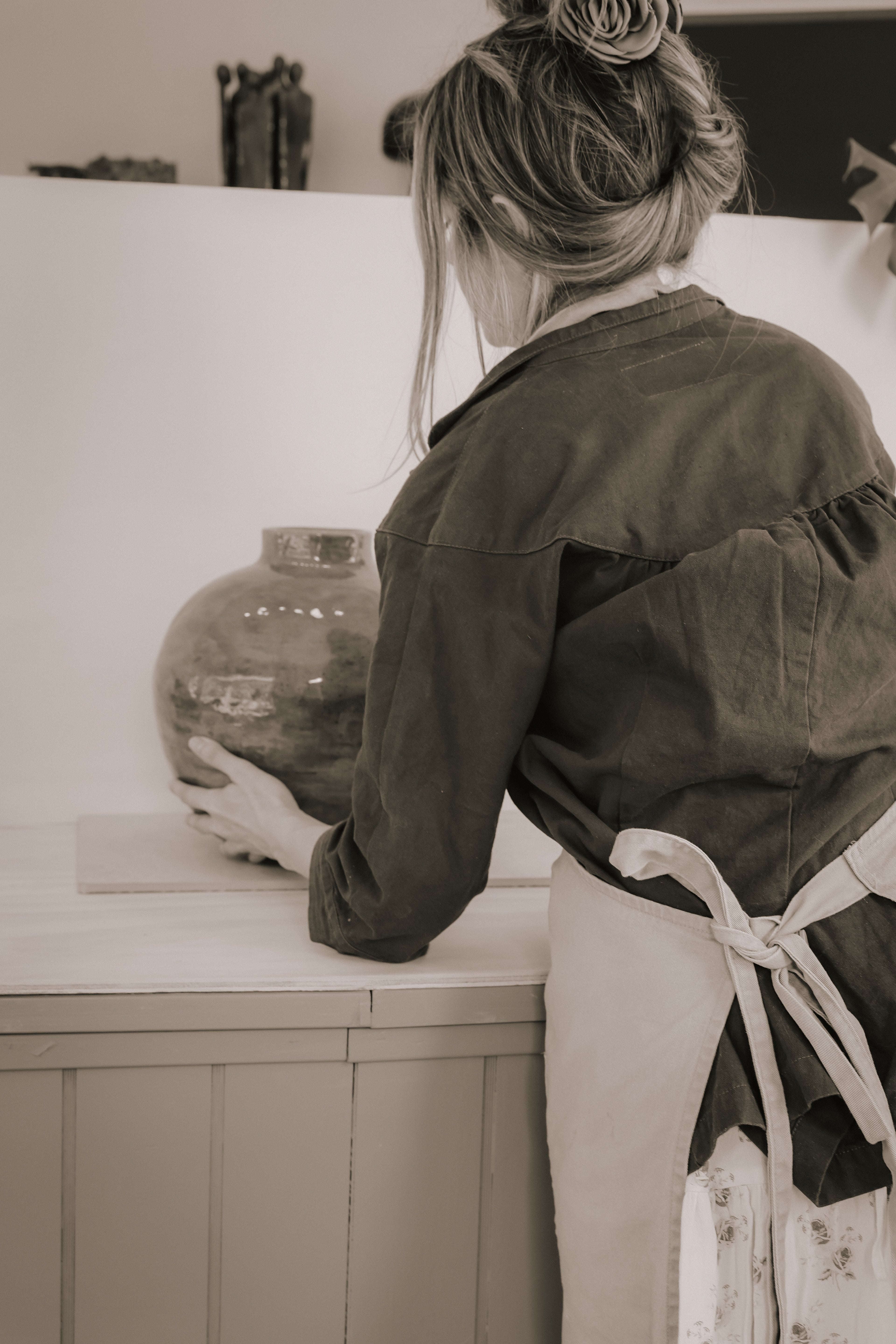 Person wearing an Lerhuset Ofelia apron holding a ceramic vase in a studio setting